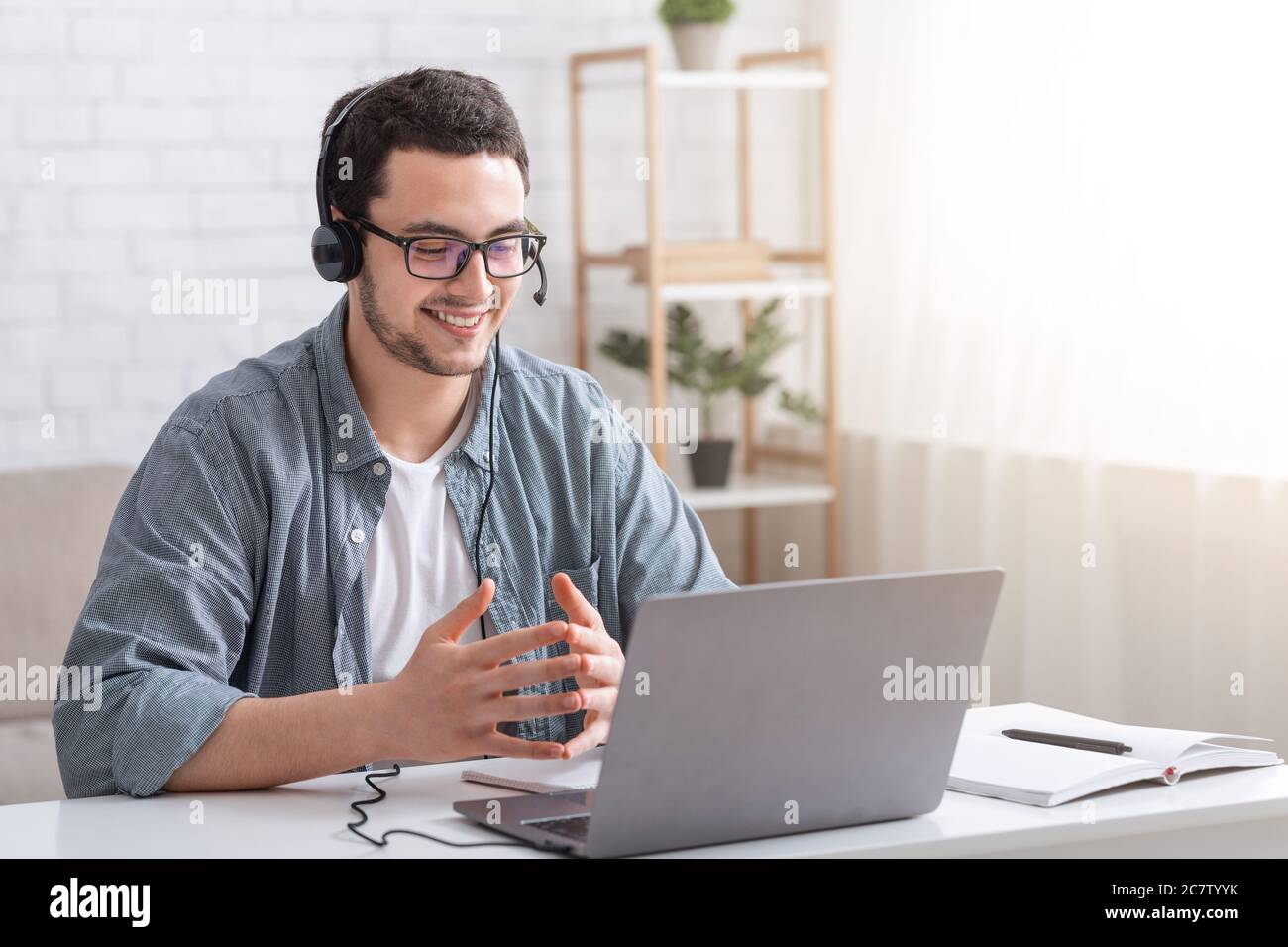 Gespräch mit dem Kunden und Videoanruf. Kerl mit Brille und Headset gestikulierend mit Händen und beobachten Laptop Stockfoto