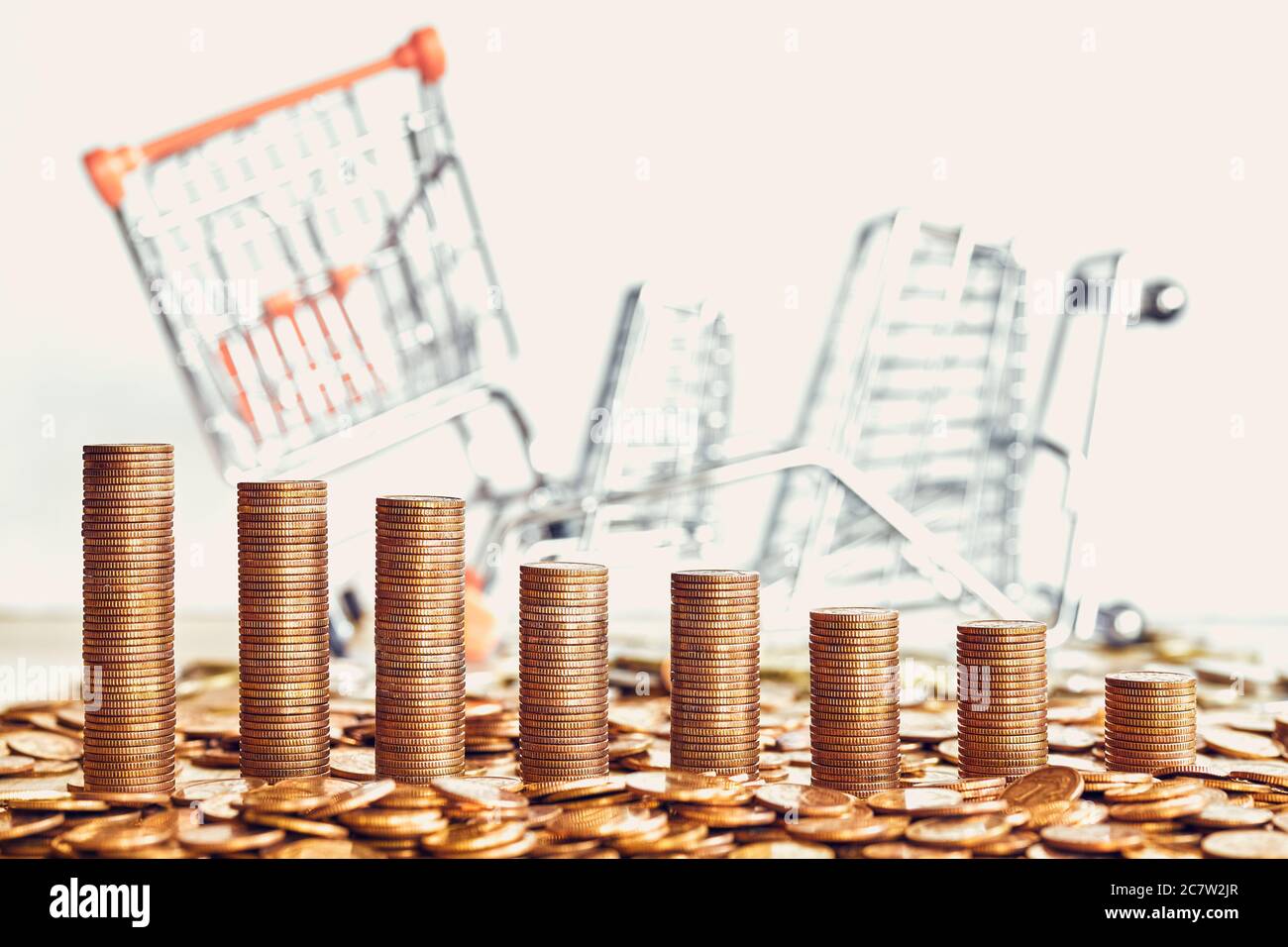 Goldene Münztürme mit gefallenen Miniatur-Einkaufswagen im Hintergrund, selektiver Fokus, Farbtonung angewendet. Stockfoto