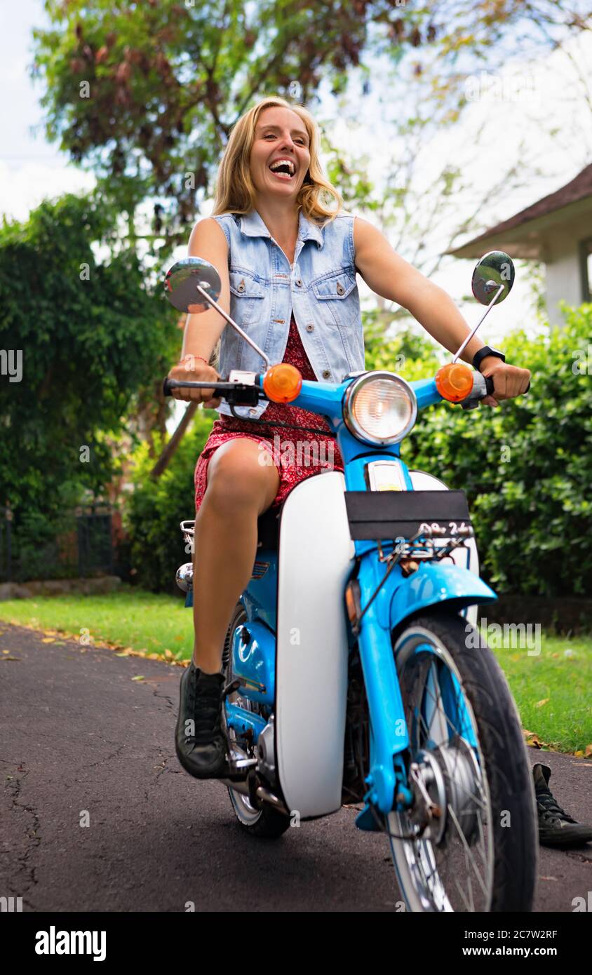 Glückliche junge Frau Fahrt auf Vermietung Custom Retro-Motorrad in Road Journey rund um tropische Insel. Reisen Abenteuer Lifestyle, Freizeitaktivitäten bei Stockfoto