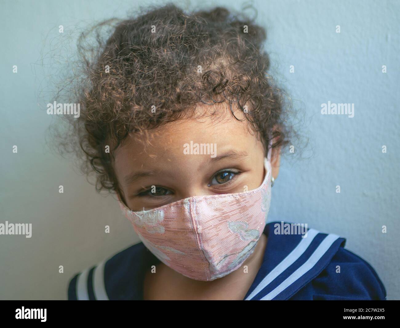 Ein kleines Mädchen mit einer Maske mit Herzen schaut auf die Kamera Stockfoto