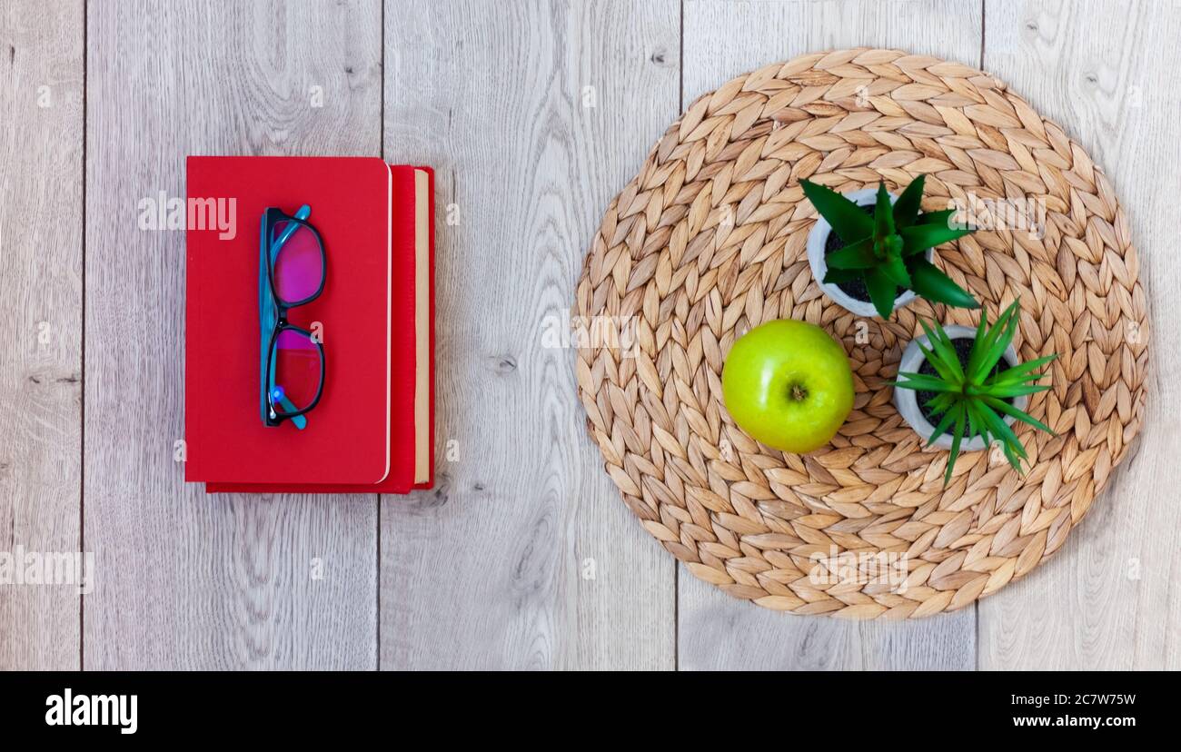 Zurück in die Schule, Stapel von Büchern in roten Abdeckungen, Gläser, grünen Apfel und Pflanzen in Töpfen auf einem Korbstand auf Holztisch. Fernunterricht. Quara Stockfoto