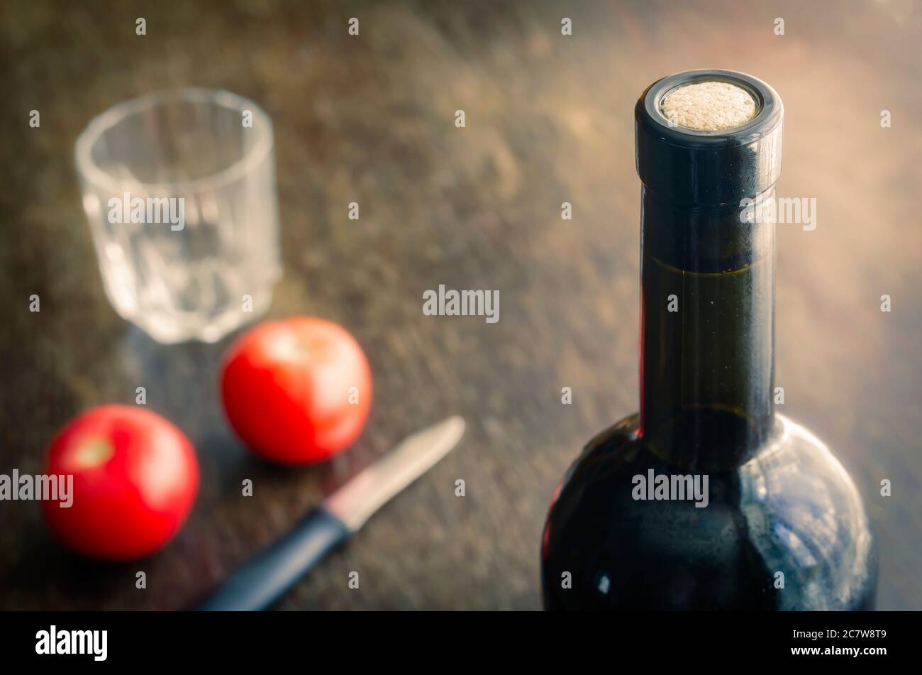 Versiegelte Flasche Rotwein auf Holztisch mit reifen Tomaten. Volle Flasche Wein mit Kork, zwei roten Tomaten, Messer und ein leeres Glas. Konzentrieren Sie sich auf die Stockfoto