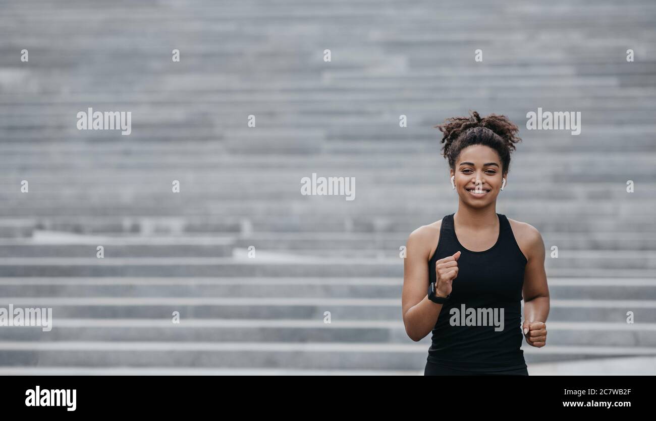 Treppenlauf in der Stadt. afroamerikanische Mädchen mit kabellosen Kopfhörern und Smart Watch Stockfoto