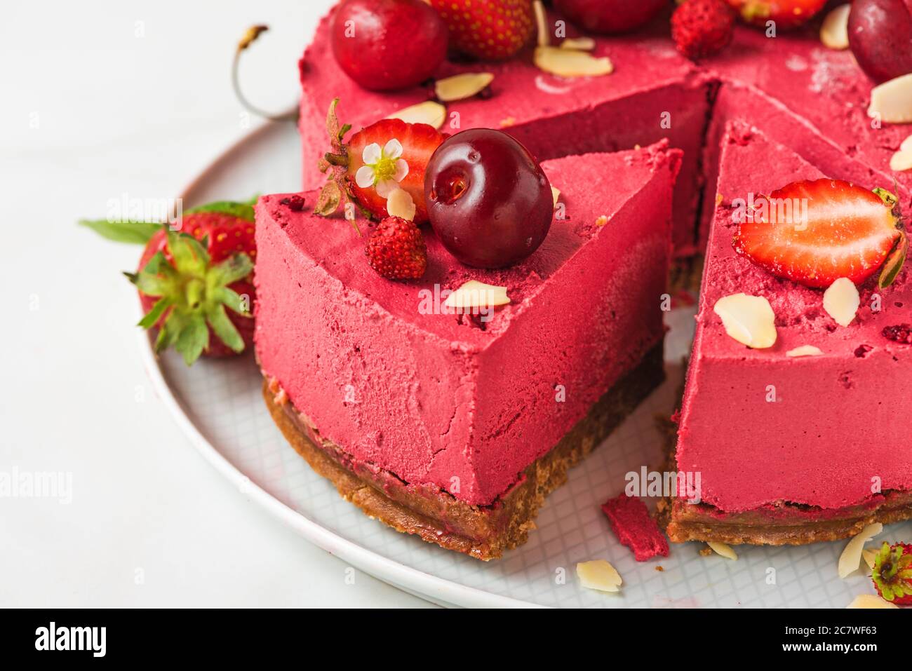 Stück Beeren veganer Käsekuchen oder Kuchen mit frischen Kirschen und Erdbeeren auf einem Teller. Nahaufnahme. Gesundes veganes Dessertgericht Stockfoto