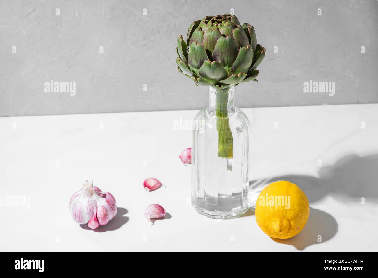Moderne minimale Nahrung Stillleben. Artischocke in einer Flasche mit Zitrone und Knoblauch auf weißem Hintergrund. Minimalkonzept Stockfoto