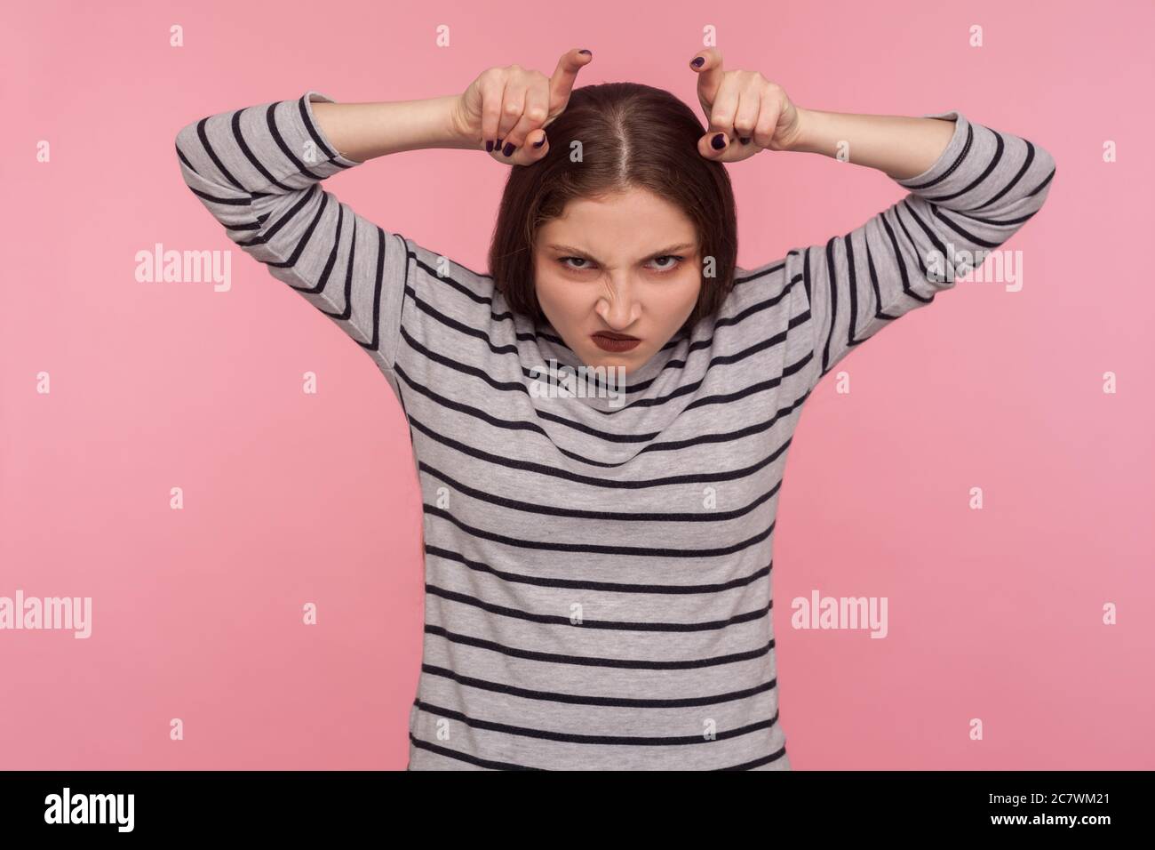 Portrait einer lustigen wütenden Frau im gestreiften Sweatshirt mit Bullhorn-Geste und mit Hasswut auf die Kamera schauend, drohende und provozierende Konflikte Stockfoto