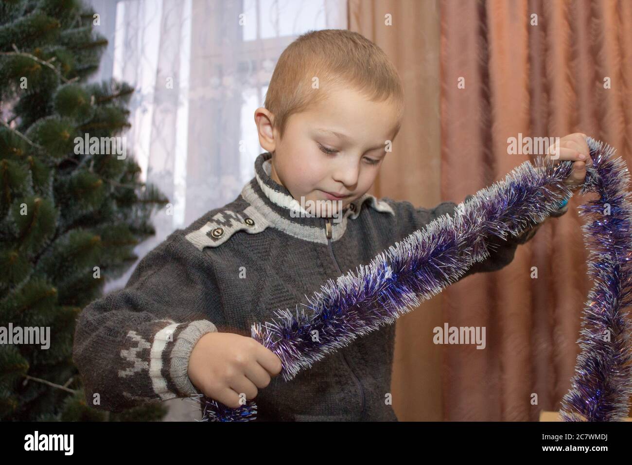 Überrascht Junge hält Lametta, um einen Weihnachtsbaum zu schmücken Stockfoto