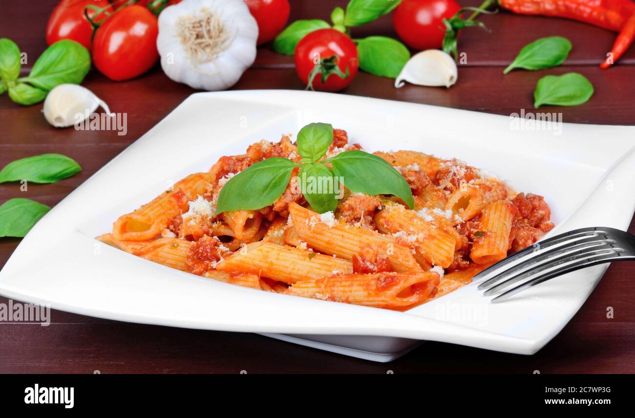 Pasta mit Tomatensauce, Parmesan und Basilikum auf einem Teller auf einem Holztisch Stockfoto