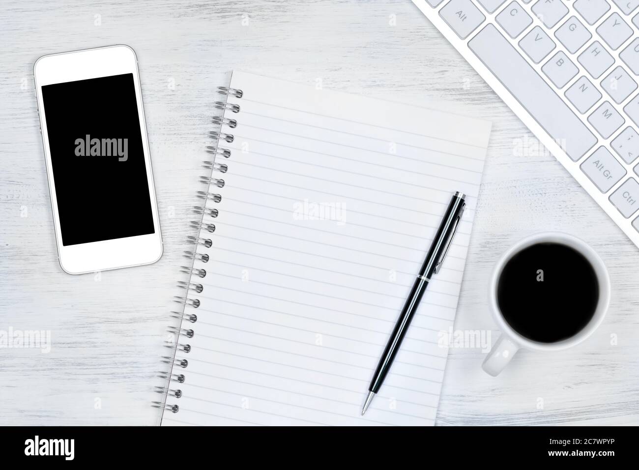 Leerer Notizblock mit Tastatur, Telefon und Kaffeetasse auf dem Schreibtisch Stockfoto