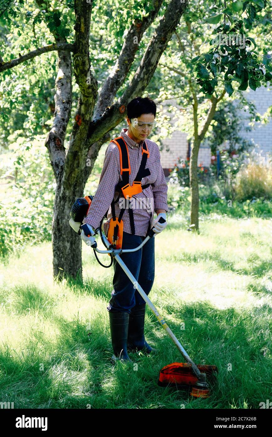 Gärtnerin mäht das Gras im Garten mit dem Schnurschneider. Gartenarbeit Konzept. Stockfoto