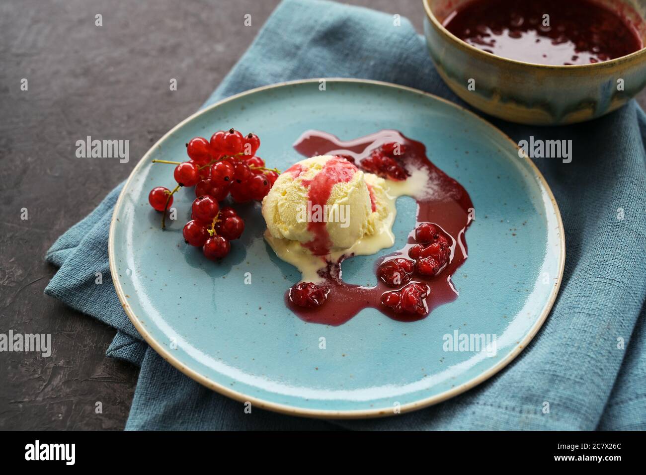 Vanilleeis mit roten Johannisbeeren und Fruchtgeleesauce auf blauem Teller, Serviette und dunklem Hintergrund mit Kopierraum, ausgewählter Fokus, enge Tiefe Stockfoto