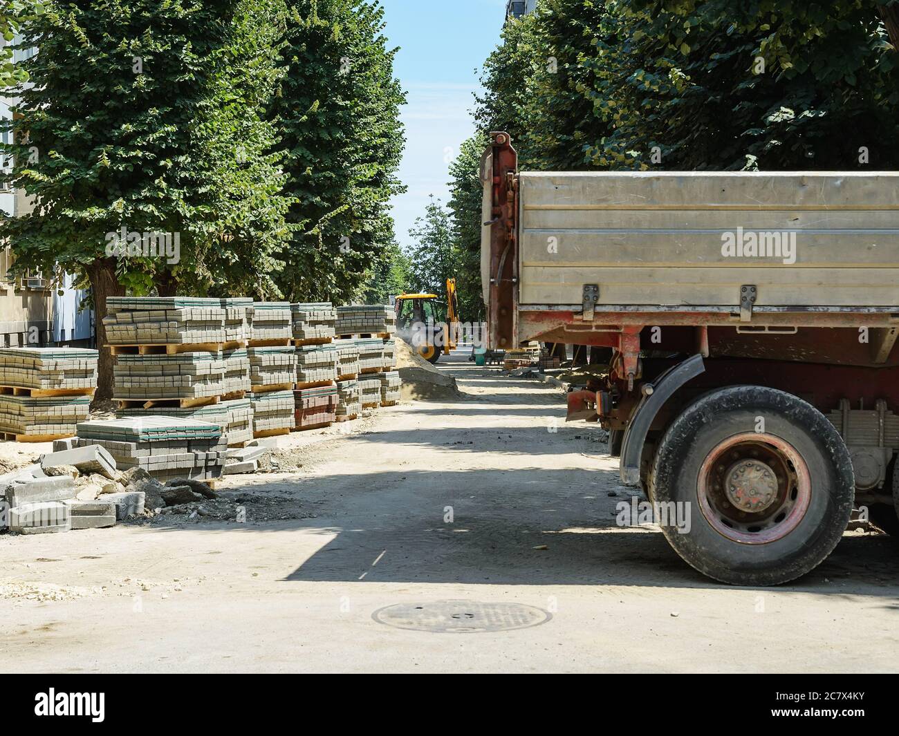 Blick auf eine schmale Stadtstraße mit grünen Bäumen bei der Reparatur der Straße und den Bürgersteig an einem sonnigen Sommertag. Verbesserung der Straßen der Stadt. Stockfoto