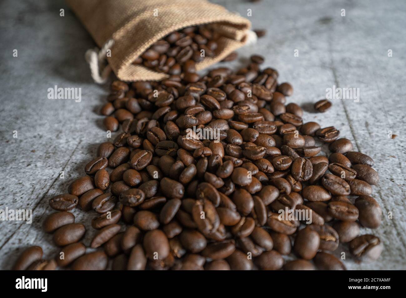 Geröstete Arabica Kaffeebohnen verteilen sich auf einem Tisch mit einem hessischen Sack im Hintergrund. Die Bohnen werden nativ auf den Philippinen angebaut. Stockfoto