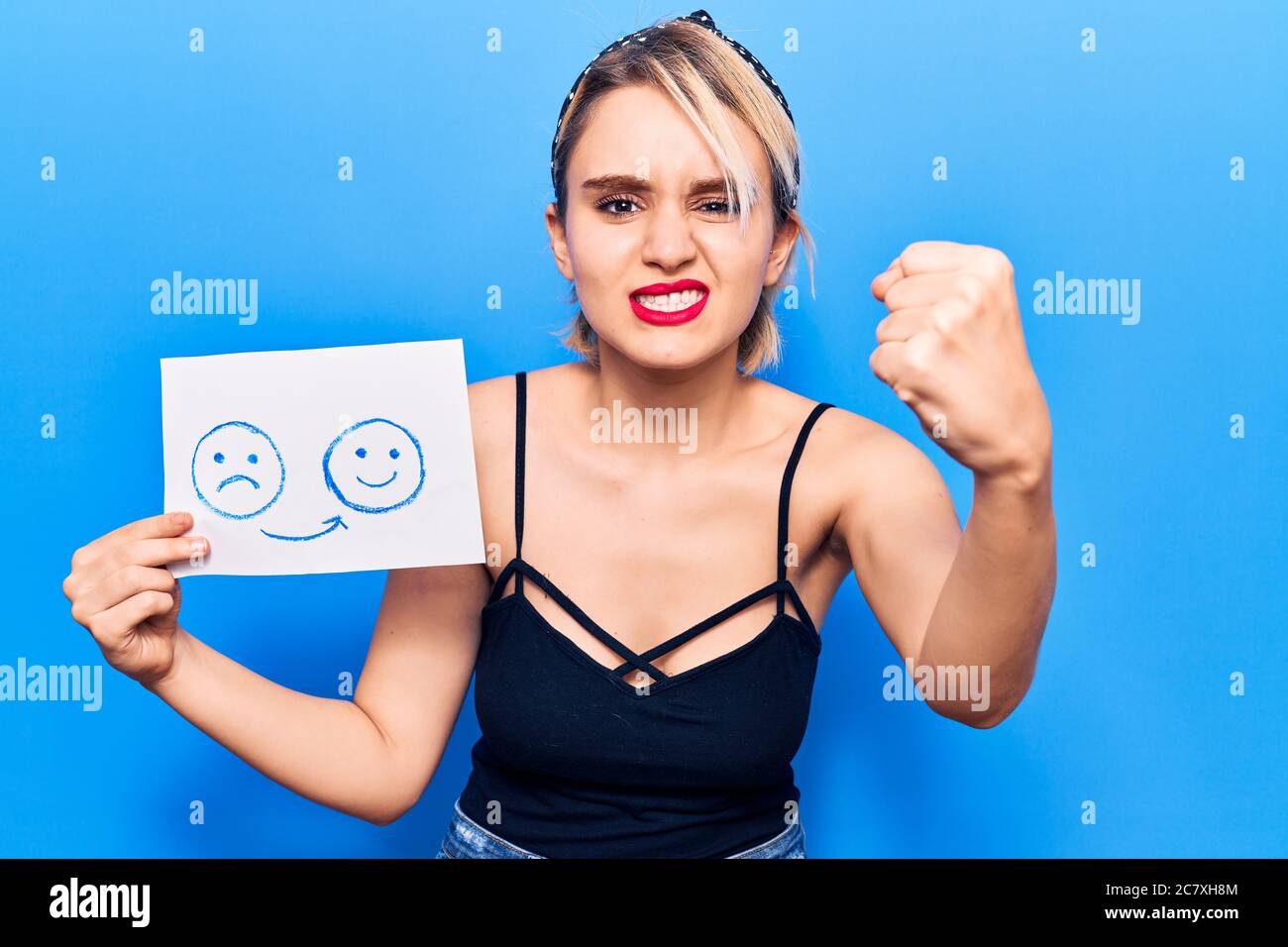 Junge schöne blonde Frau hält traurig bis glücklich Emotion Papier verärgert und frustriert schreien vor Wut, schreien verrückt mit Wut und Hand angehoben Stockfoto