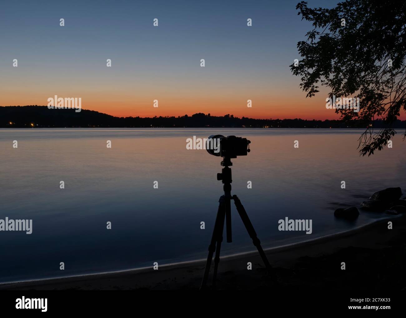 Eine Kamera und ein Stativ am Ufer des Chemong Lake bei Peterborough sind bereit, Kometenneuland mit einem wunderschönen blauen und orangen Sonnenuntergang zu fotografieren. Stockfoto