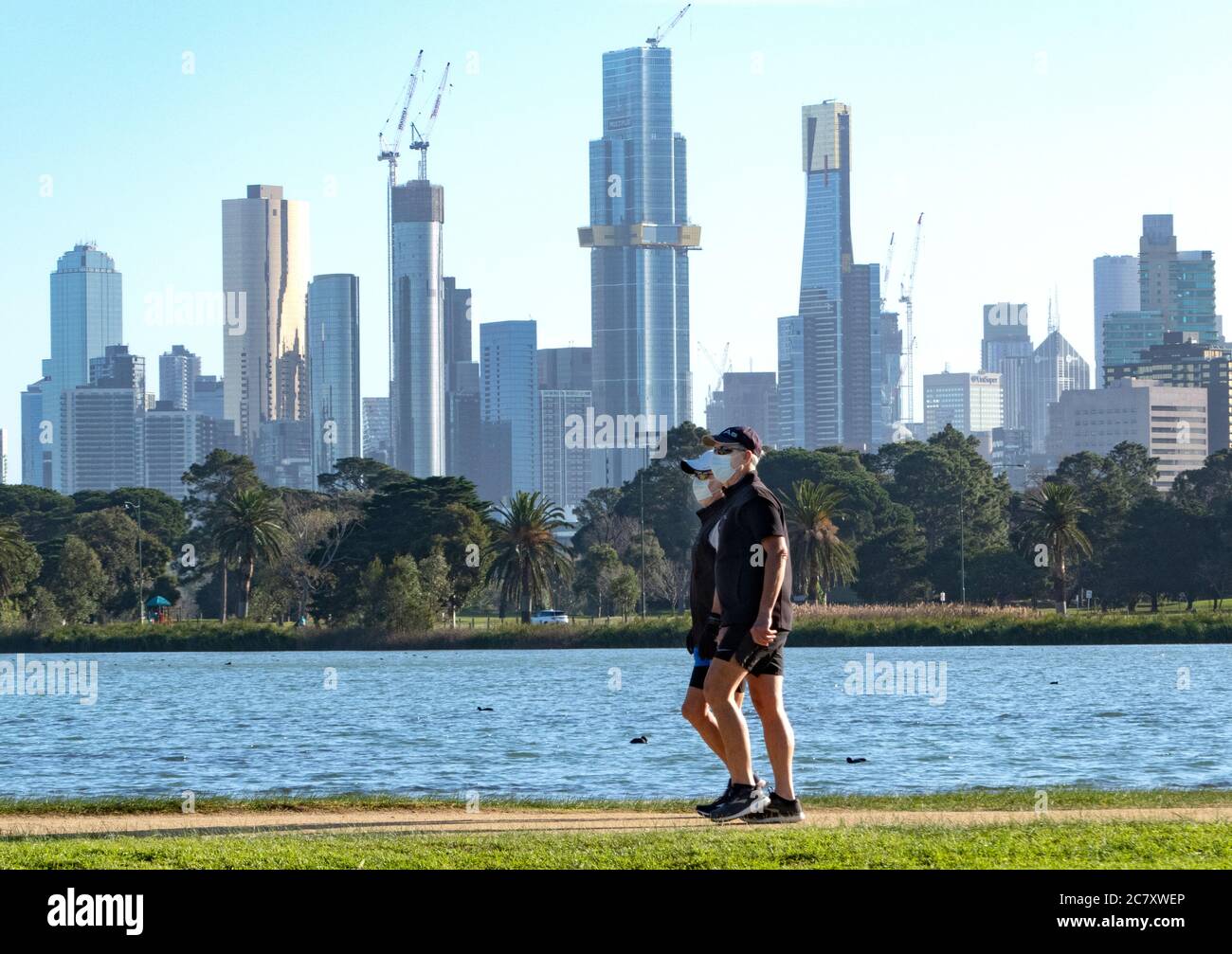 Coronavirus Melbourne Covid-19. Menschen mit Schutzmaske laufen durch Melbourne mit der Skyline der Stadt im Hintergrund. Stockfoto