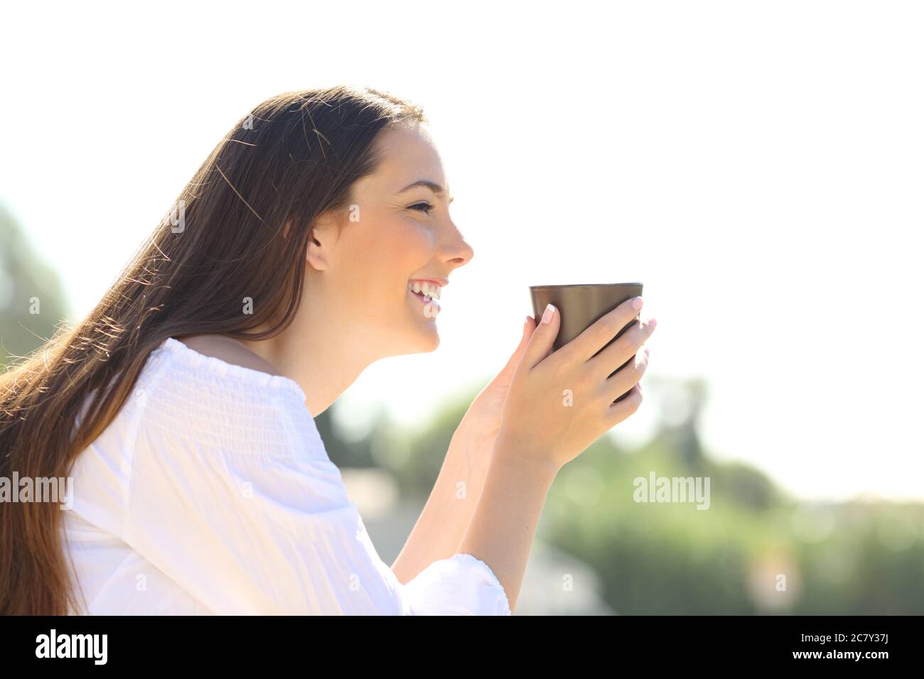 Seitenansicht einer glücklichen Frau, die eine Kaffeetasse hält und draußen die Aussicht betrachtet Stockfoto