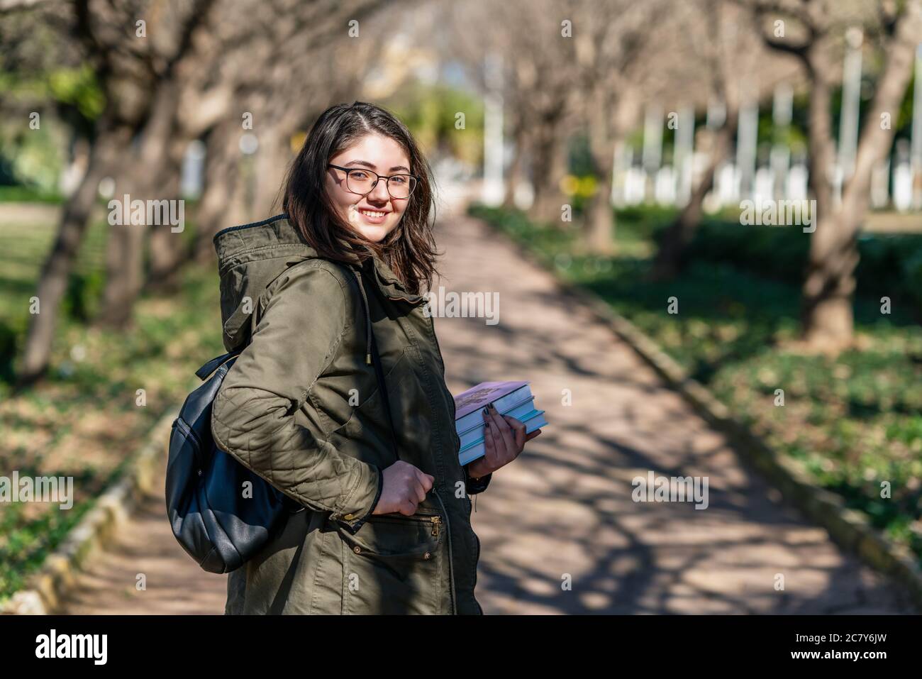 Intellektuelles junges Mädchen bleibt und schaut auf jemanden in einem Park mit einigen Büchern in ihren Händen. Hochwertige Fotos Stockfoto