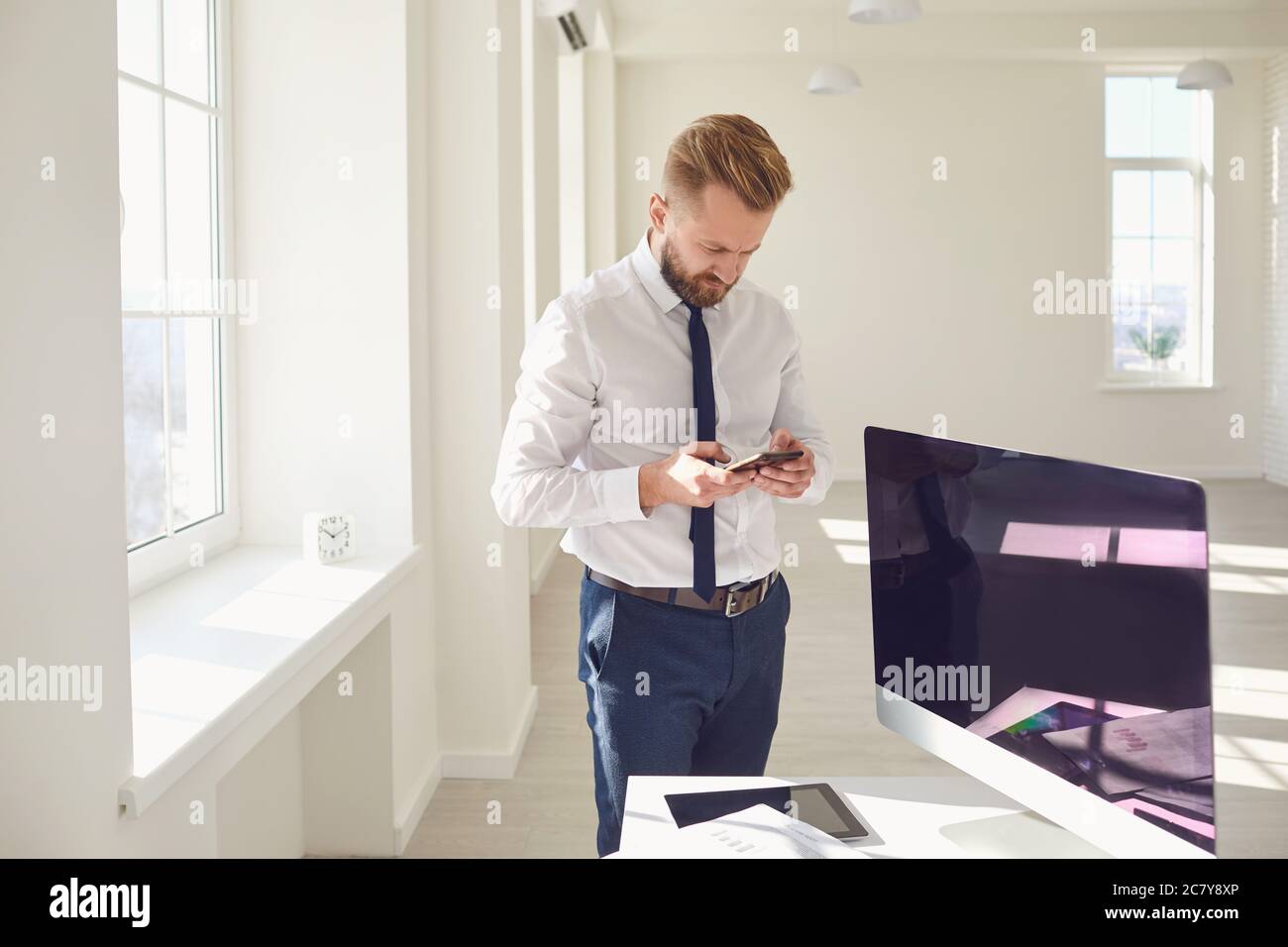 Ein bärtiger Geschäftsmann liest SMS-Text, während er am Arbeitsplatz im Büro steht. Stockfoto