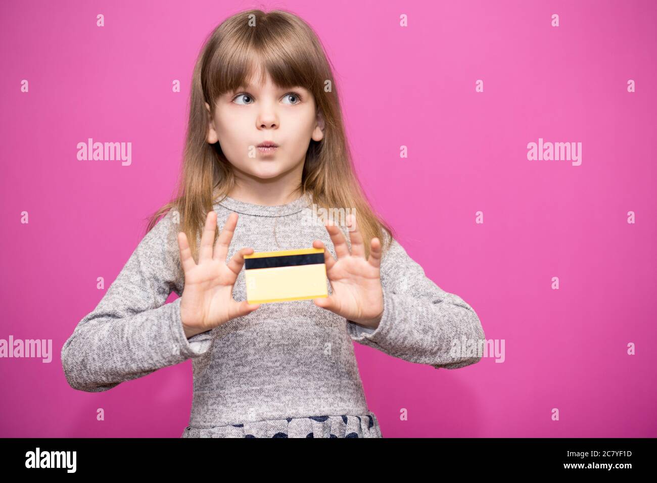 Fröhliche kleine blonde Mädchen 6-7 Jahre alt mit überrascht Gesicht halten Kreditkarte auf rosa isoliert. Lifestyle-Konzept für die Kindheit. Stockfoto