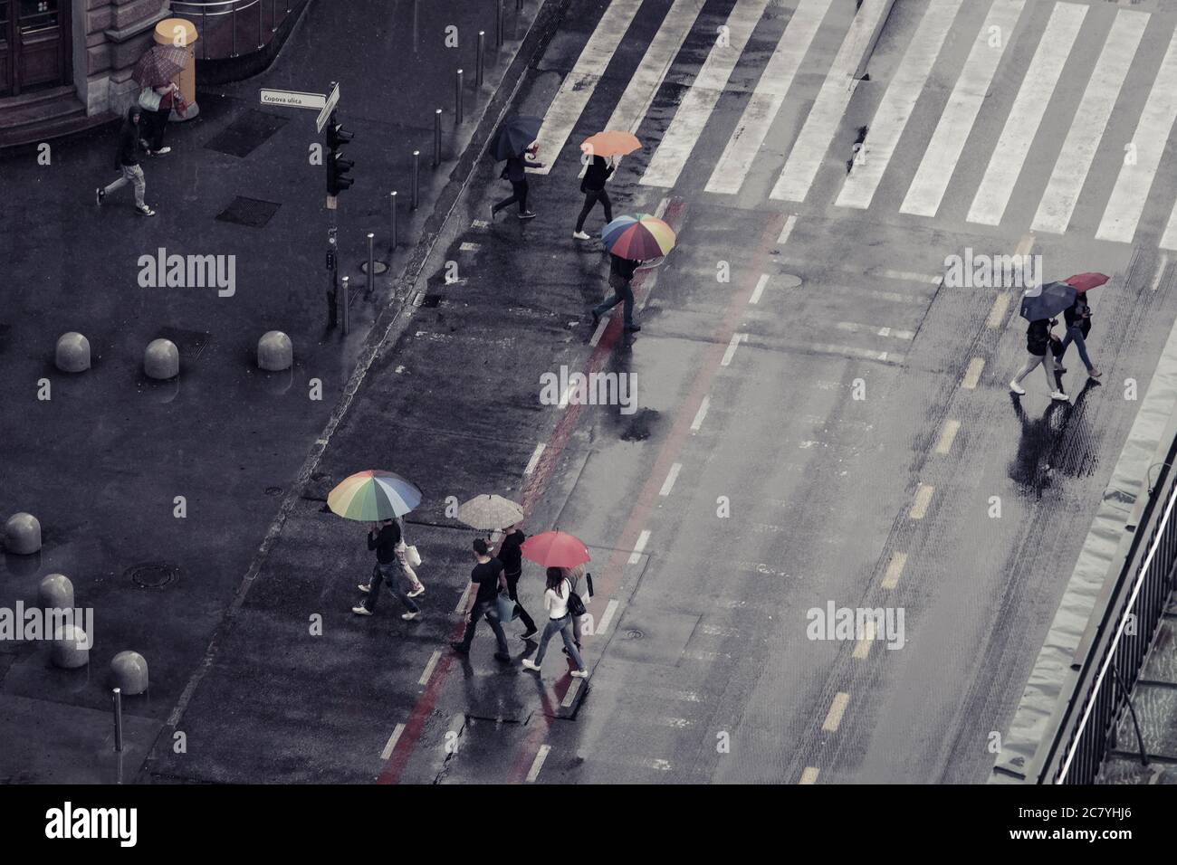 Draufsicht auf eine regnerisch-nasse Straße mit Kreuzwalken und Fußgängern mit bunten, offenen Sonnenschirmen Stockfoto