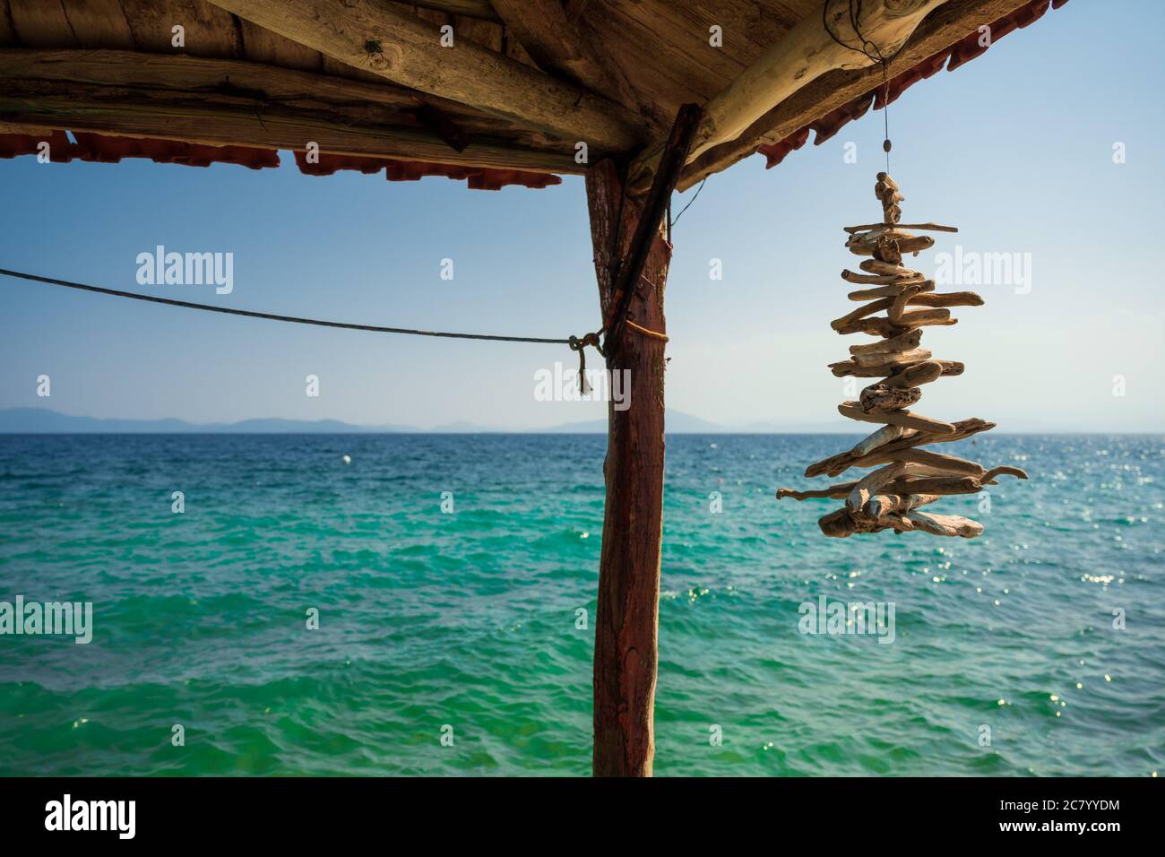 Dekorative kleine Treibholzstücke hängen als Windspiel vom Sonnenschirm mit dem blauen Meer im Hintergrund. Stockfoto