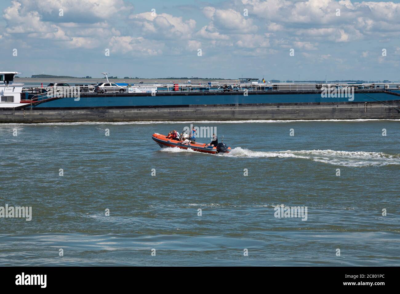 Terneuzen, Niederlande, 12. Juli 2020, ein orangefarbenes Gummiboot mit sechs Personen segelt neben einem großen Schiff Stockfoto