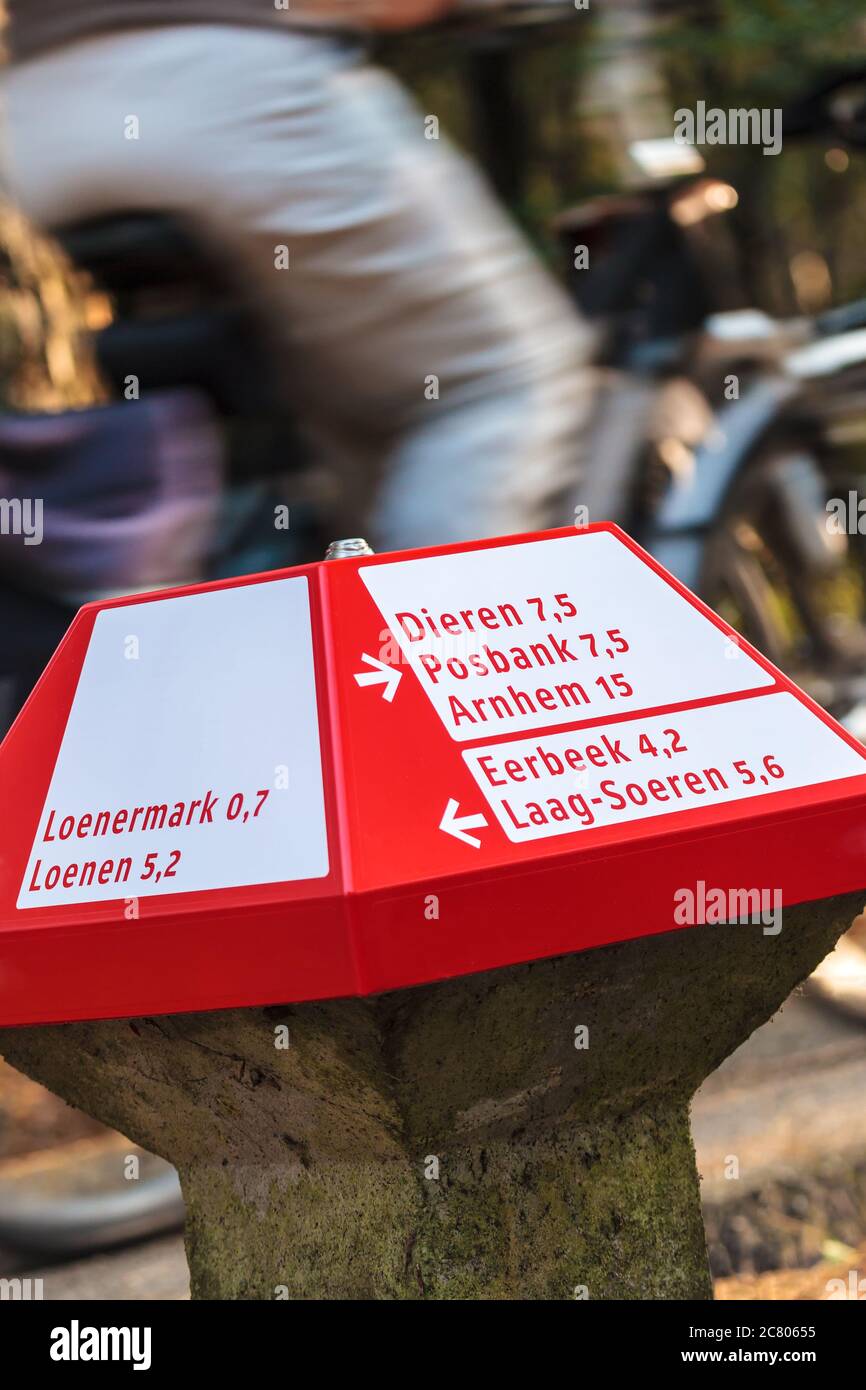Ein rotes Radwegschild im niederländischen Nationalpark Veluwe mit einem Radfahrer im Rücken Stockfoto