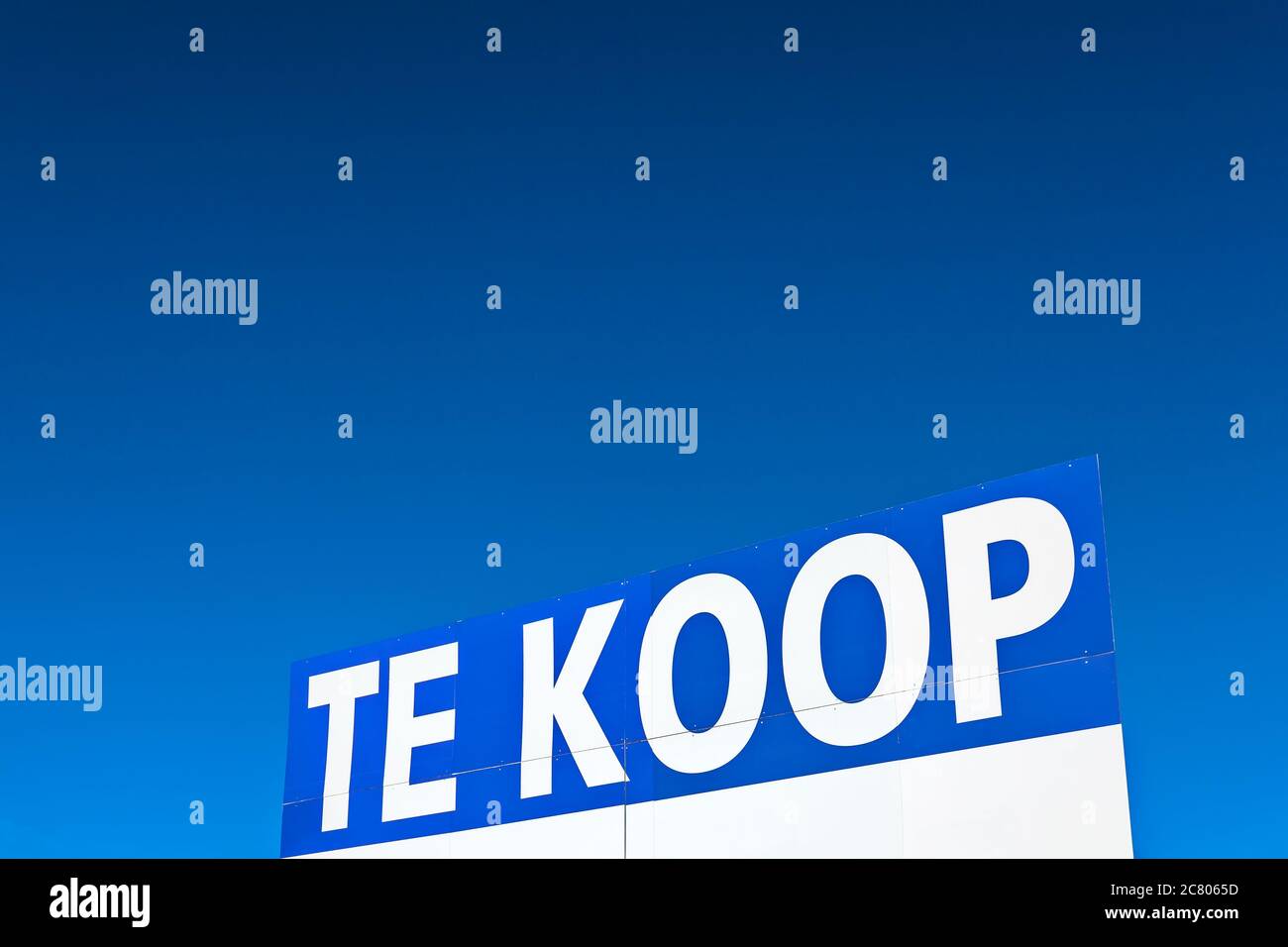 Großes Immobilienschild mit dem niederländischen Text "zum Verkauf" vor einem klaren blauen Himmel Stockfoto
