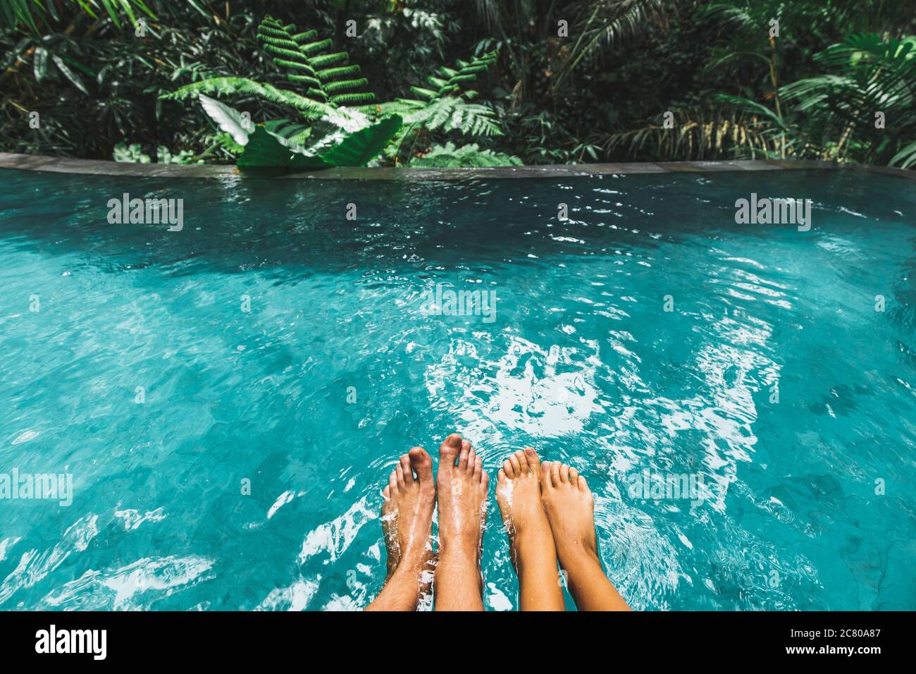 Paar Füße zusammen in Luxus-Pool mit türkisfarbenem klarem Wasser im Freien mit Blick auf den Dschungel. Tropische Flitterwochen, Urlaub. Stockfoto