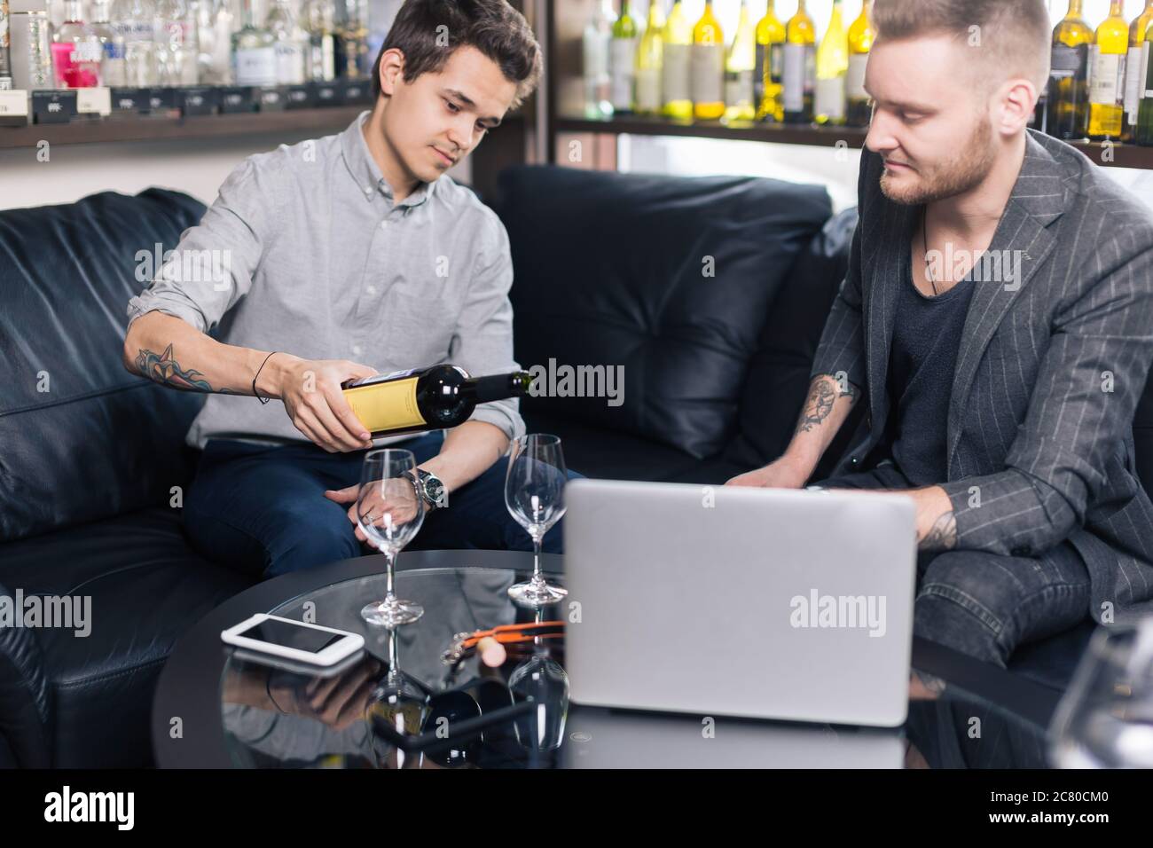 Zwei junge Männer gießen Wein und lächeln Stockfoto