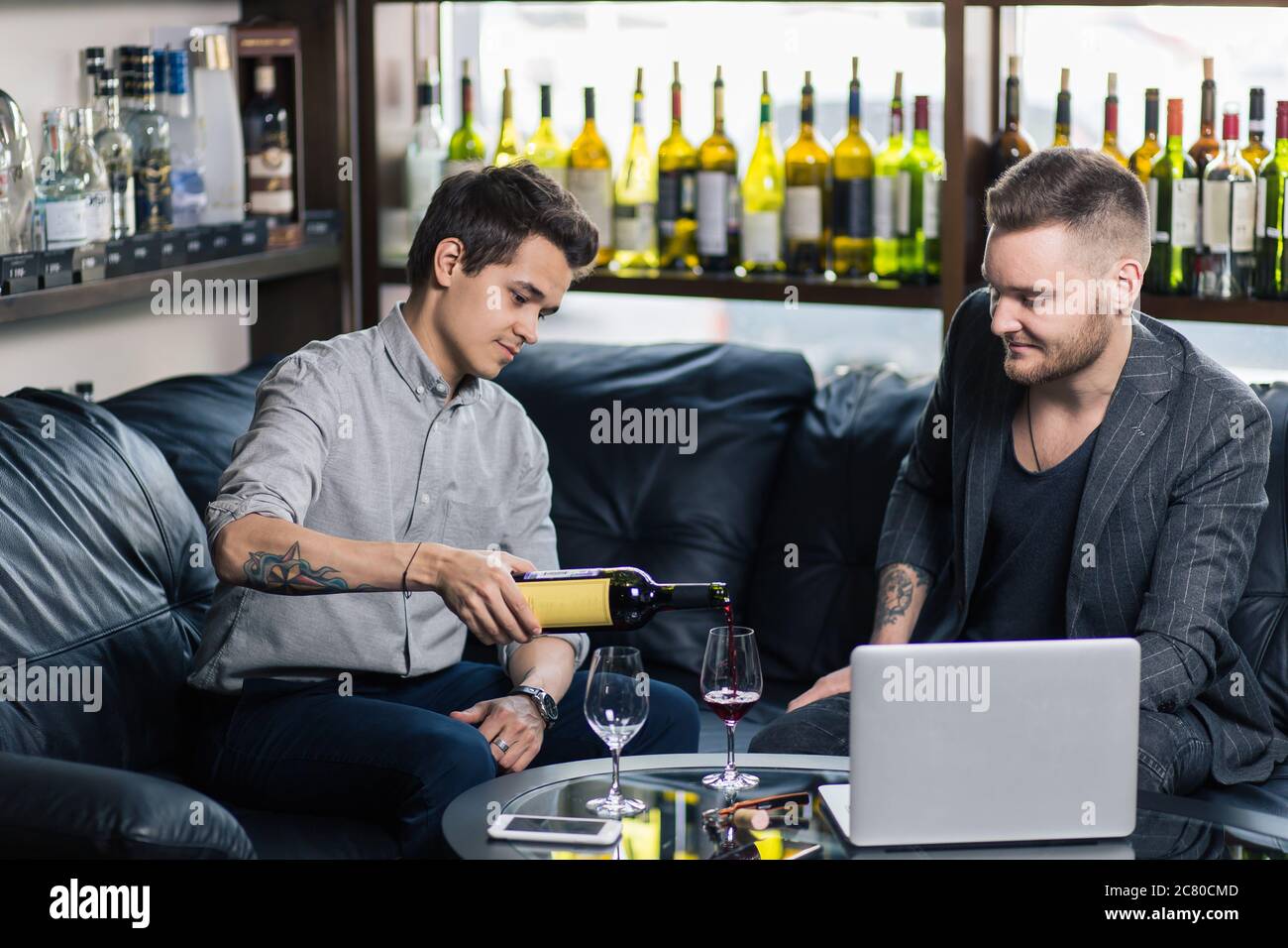 Zwei junge Männer gießen Wein und lächeln Stockfoto
