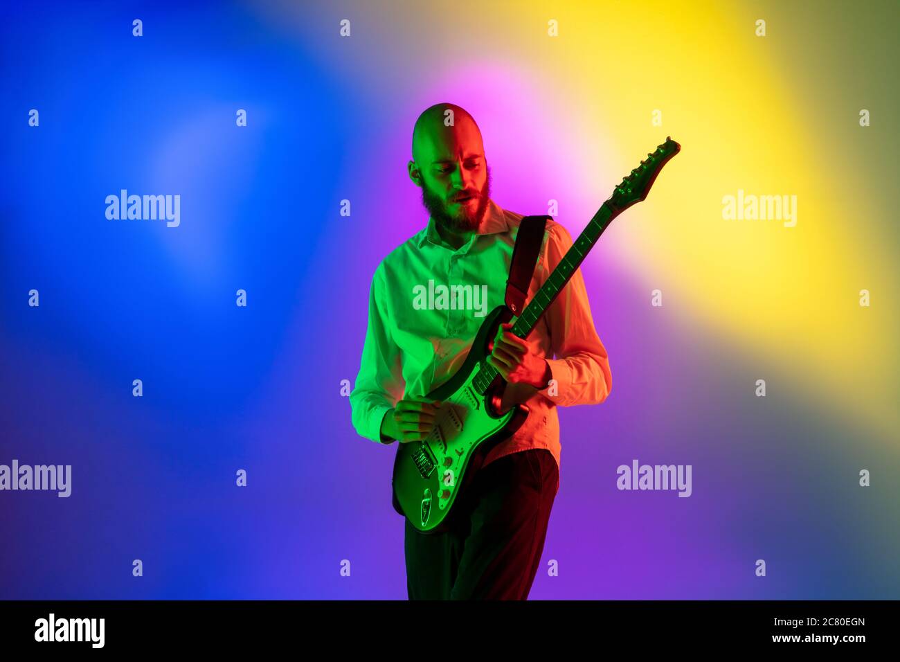 Gespannt. Junge kaukasische inspirierte und expressive Musiker, Gitarrist auf bunten Hintergrund in Neon. Konzept der Musik, Hobby, Festival, Kunst. Fröhliche Künstler, bunt, helles Porträt. Stockfoto