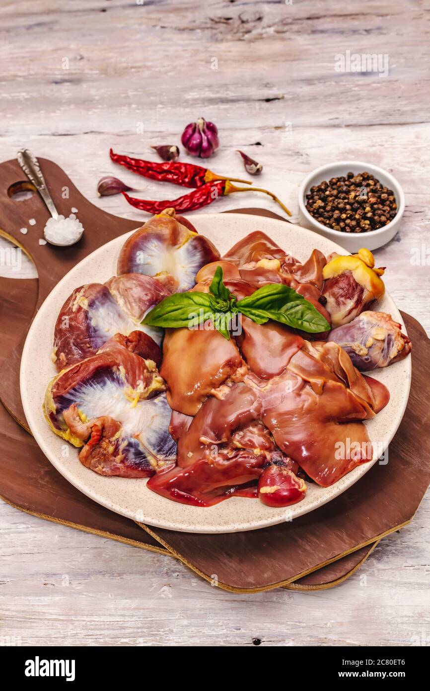 Frische rohe Hühnerfleisch: Herz, Leber, Magen. Trockene Gewürze, Meersalz, Chili. Weiße Holzbretter Hintergrund, Nahaufnahme Stockfoto