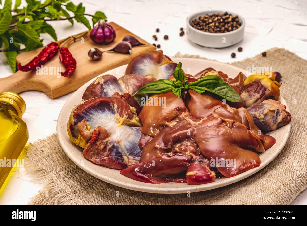 Frische rohe Hühnerfleisch: Herz, Leber, Magen. Trockene Gewürze, Meersalz, Chili, Olivenöl, frische Minze. Weißer Kitt Hintergrund, Nahaufnahme Stockfoto
