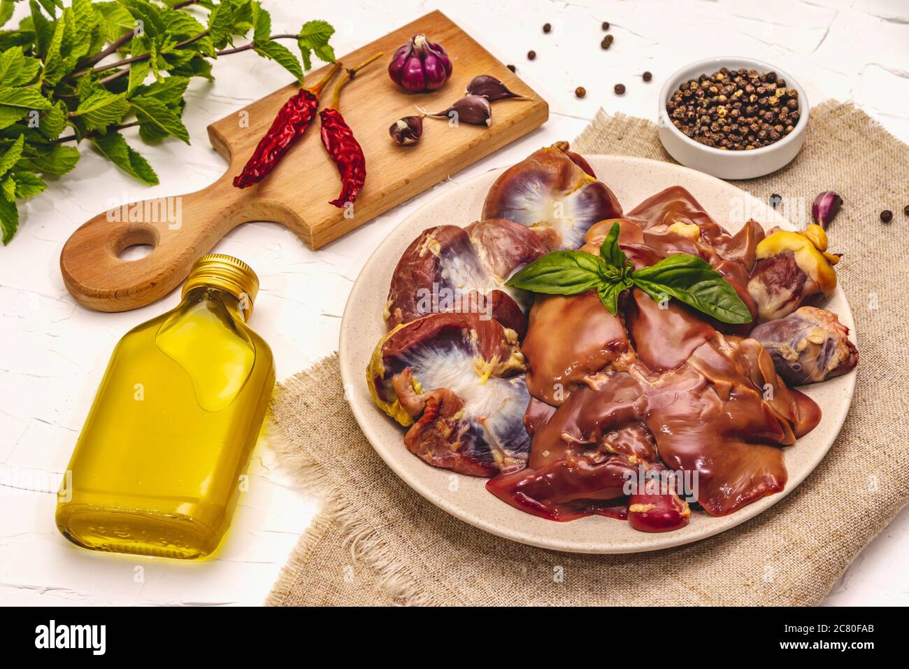 Frische rohe Hühnerfleisch: Herz, Leber, Magen. Trockene Gewürze, Meersalz, Chili, Olivenöl, frische Minze. Weißer Kitt Hintergrund, Nahaufnahme Stockfoto
