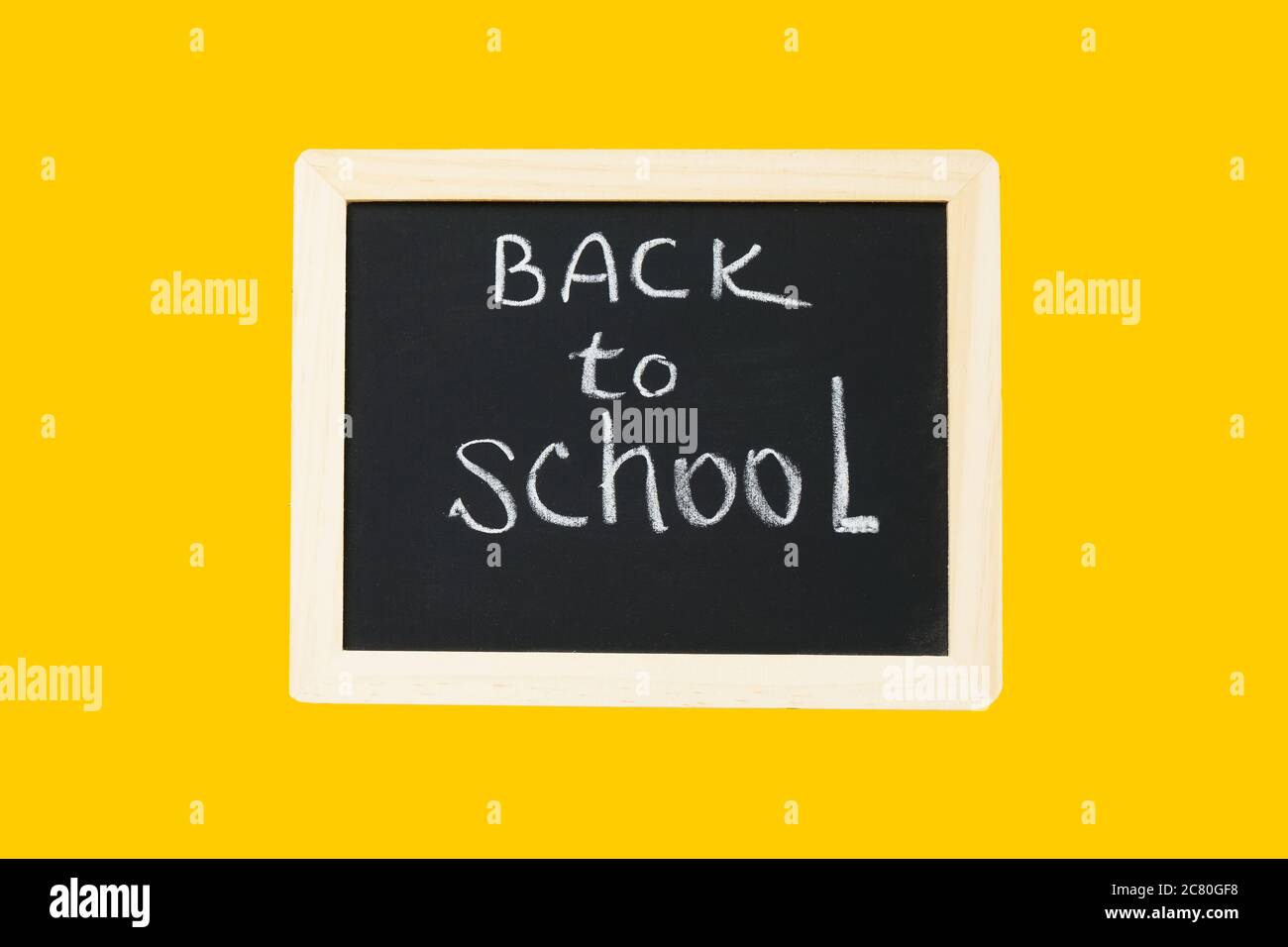 Zurück zur Schule Konzept. ZURÜCK IN DIE SCHULE geschrieben auf einer schwarzen Tafel auf gelbem Hintergrund. Flach liegend, Kopierplatz Stockfoto