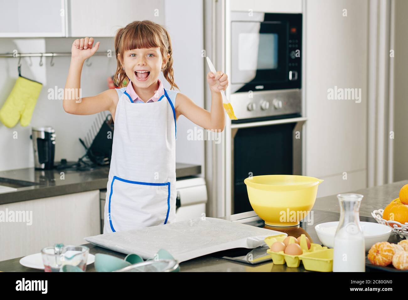 Portrait von glücklich aufgeregt kleines Mädchen mit Silikon-Pinsel in der Hand genießen Backwaren zu Hause Stockfoto
