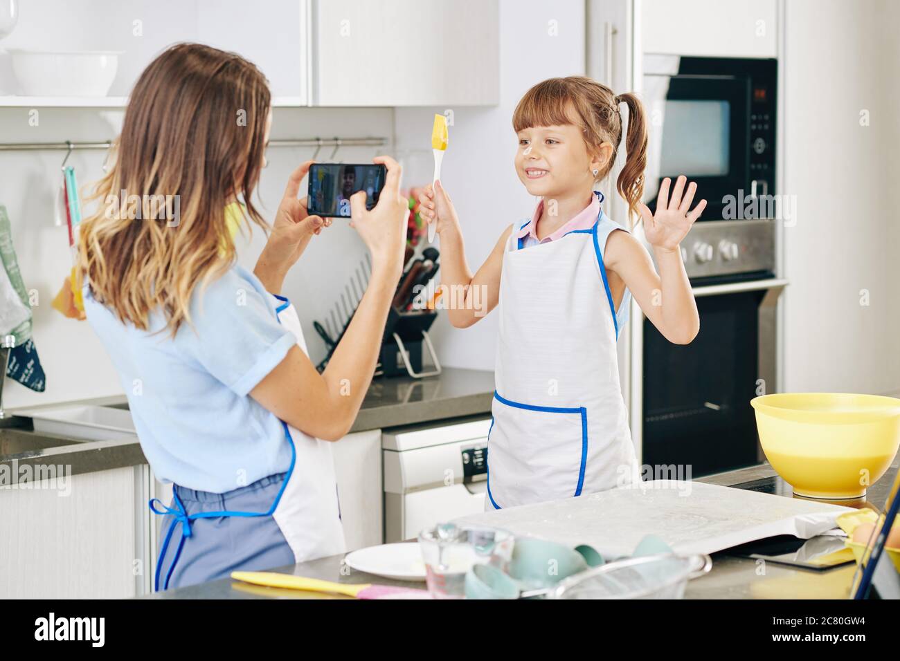 Junge Frau, die ihre Tochter oder Schwester mit Silikonbürste in der Küche fotografiert, wenn sie zusammen backen Stockfoto