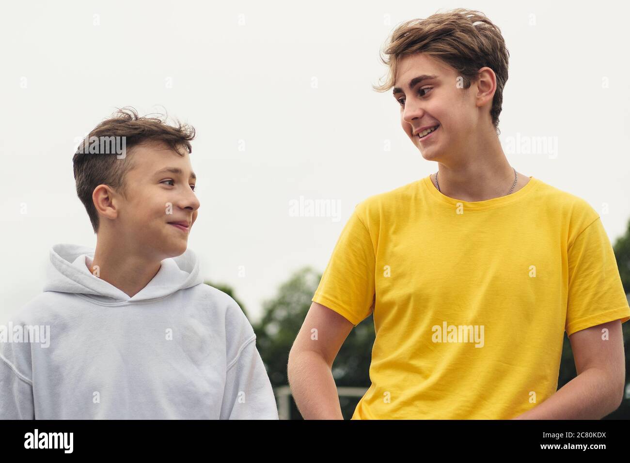 Zwei glückliche junge Teenager-Jungen oder Brüder stehen im Freien in einer Nahaufnahme niedrigen Winkel Blick gegen einen grauen High Key Himmel zu plaudern Stockfoto