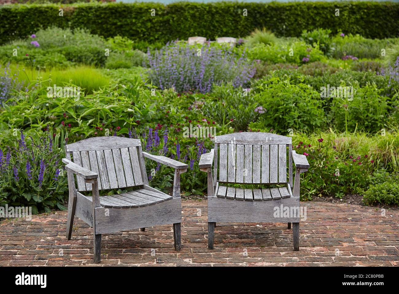 Zwei Holzgartenstühle auf gepflasterter Terrasse in der ummauerten Garten in Scampston Hall Stockfoto