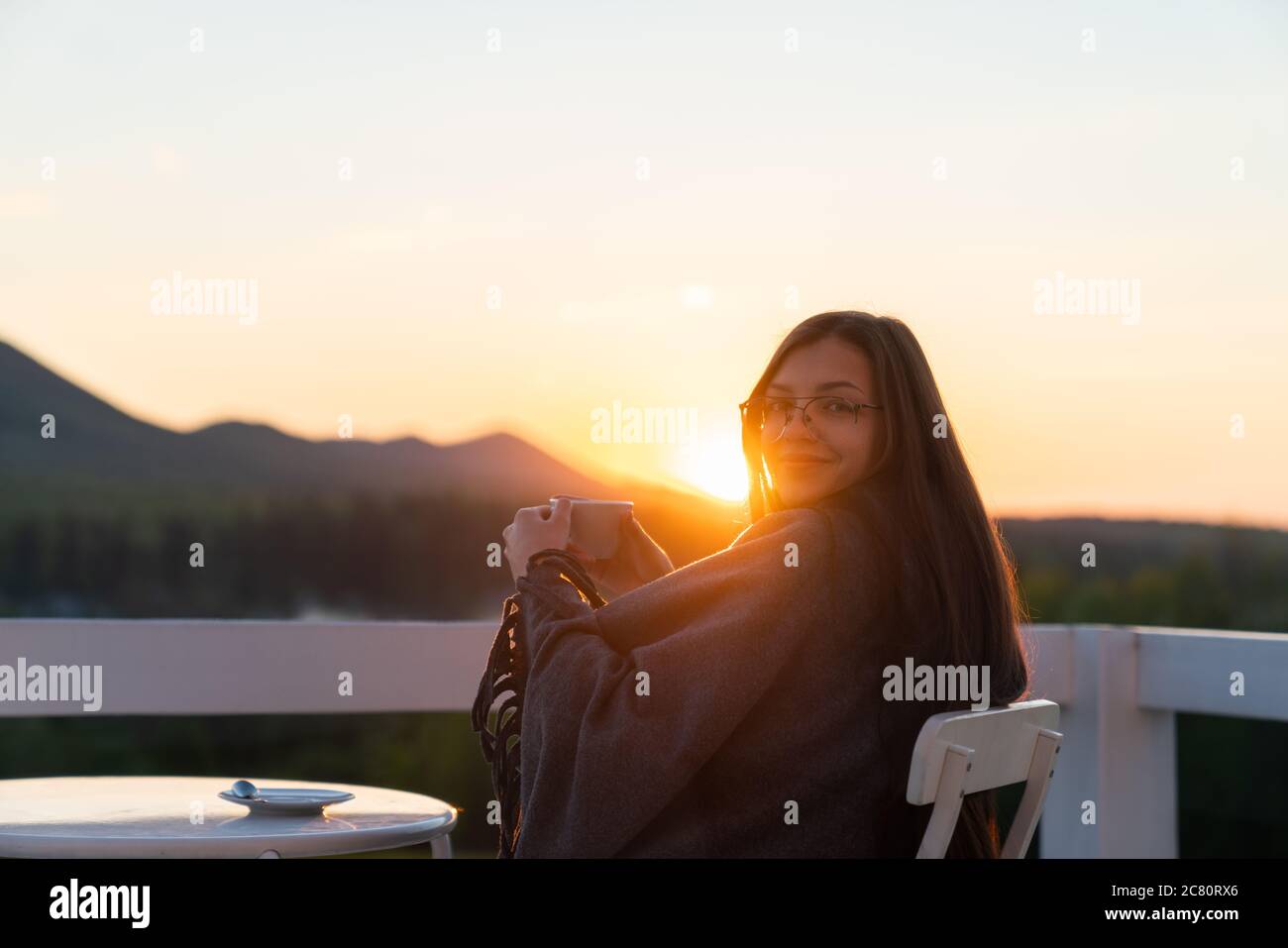 Junge Frau trinkt heißen Kaffee auf dem Balkon mit schöner Berglandschaft Stockfoto