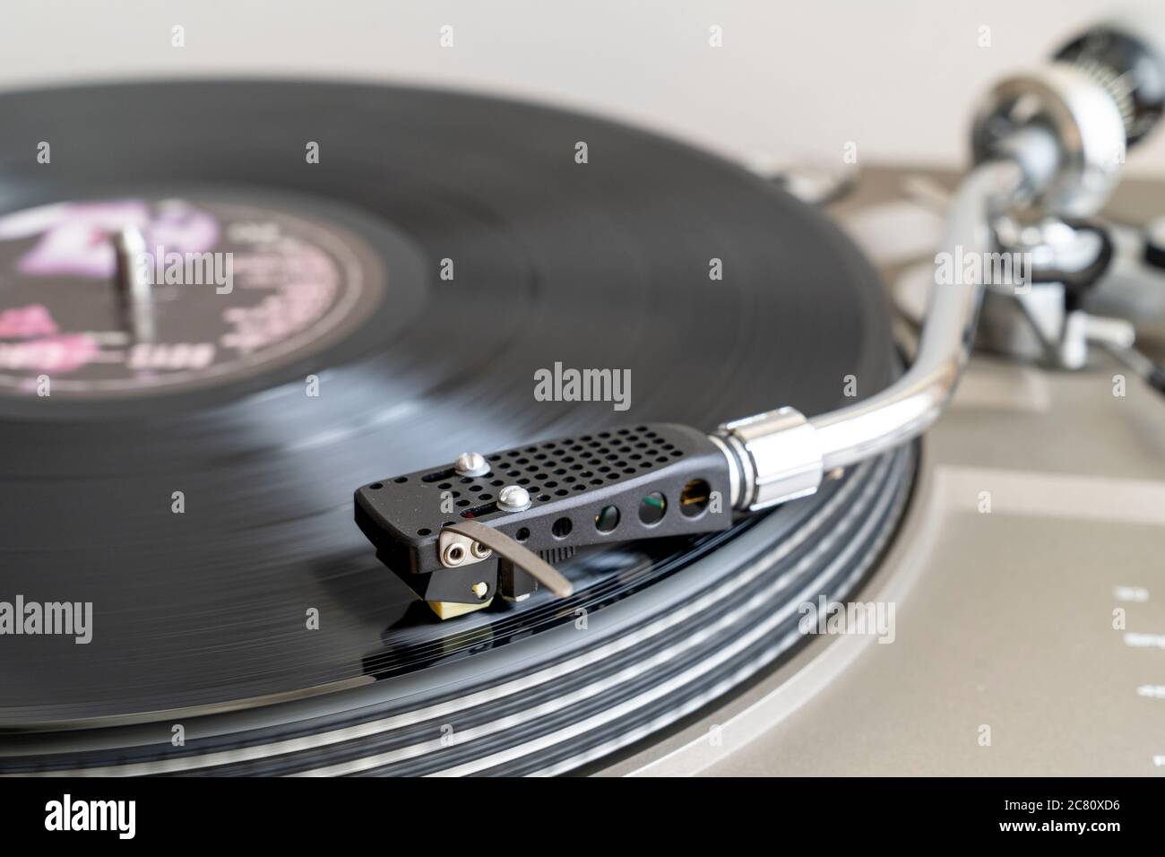 Nahaufnahme eines Plattendecks mit S-förmigem Tonarm mit Stylus, der LP-Vinyl-Schallplatte auf Bandantrieb-Plattenspieler spielt. Bewegungsunschärfe. Einfacher Hintergrund. Stockfoto