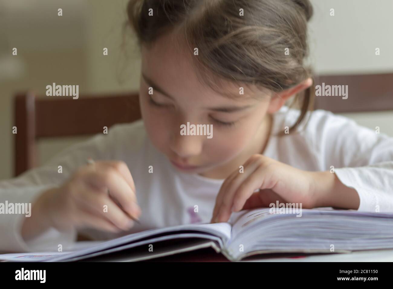 Grundschülerin macht ihre Hausaufgaben. Sie macht ihre eigenen Hausaufgaben allein zu Hause, weil die Schulen wegen der Corona pandemi geschlossen sind Stockfoto