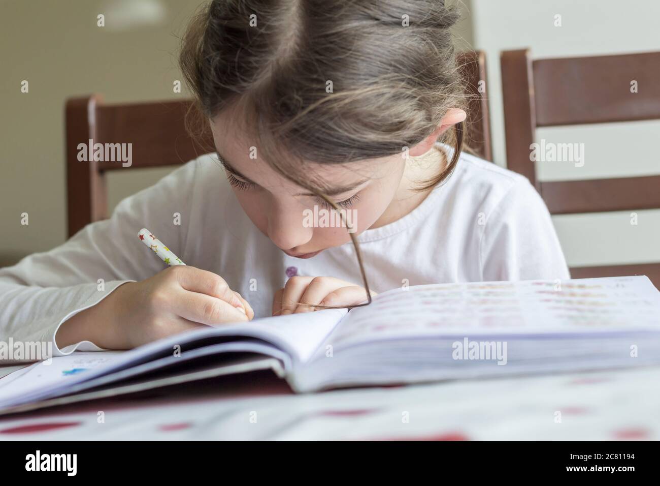Grundschülerin macht ihre Hausaufgaben. Sie macht ihre eigenen Hausaufgaben allein zu Hause, weil die Schulen wegen der Corona pandemi geschlossen sind Stockfoto