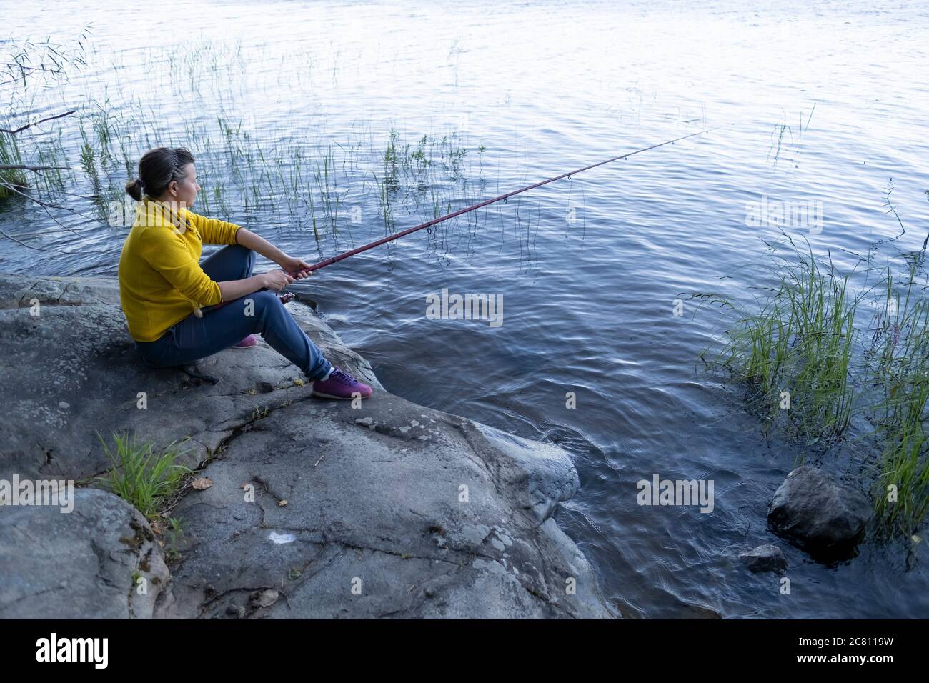 Fischerfrau sitzt auf Stein in der Nähe des Sees Stockfoto