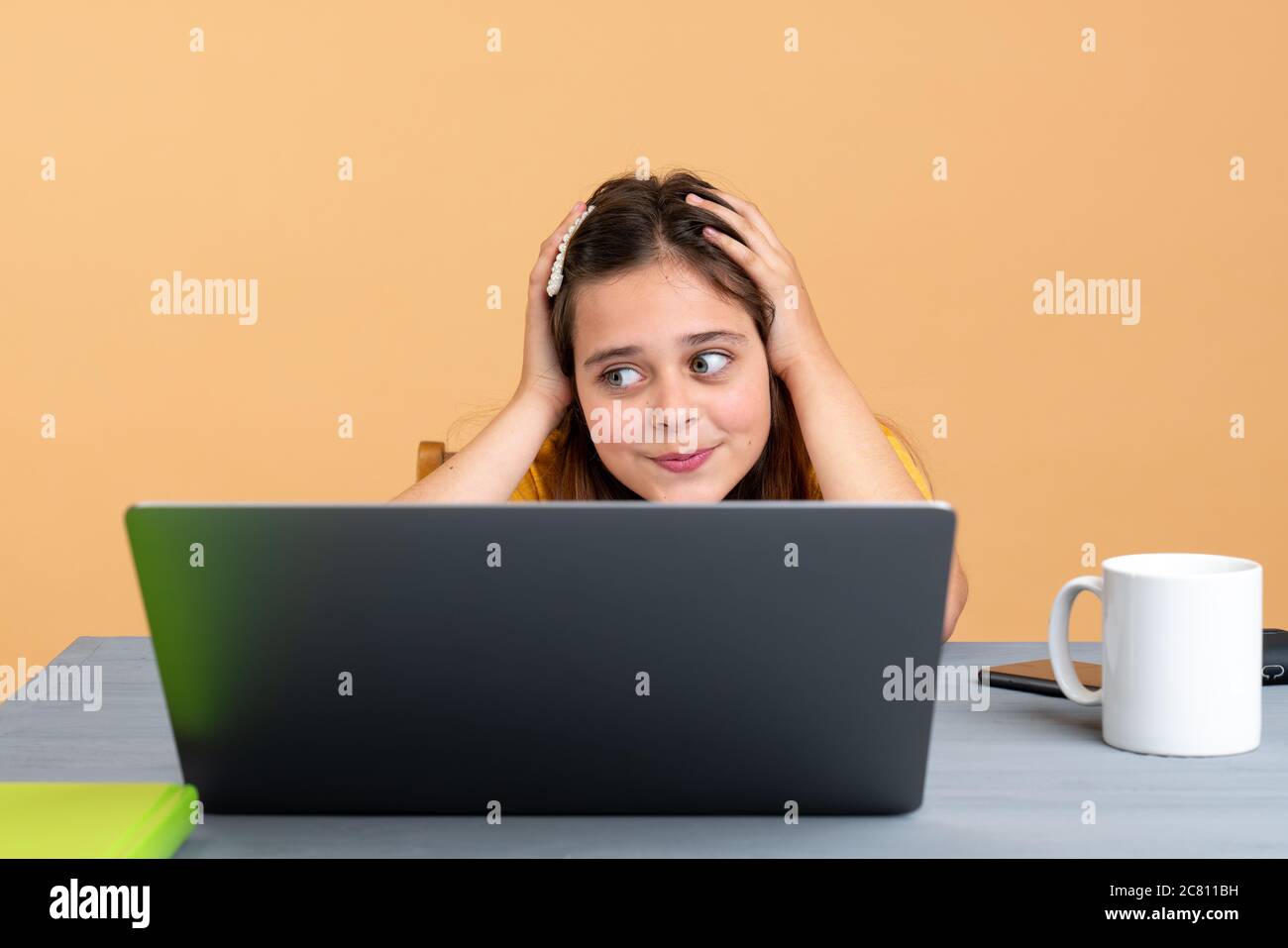 Erschöpftes Schulkind, das am Schreibtisch neben dem Laptop sitzt und ein Buch kopiert, während es zu Hause Schularbeiten macht Stockfoto