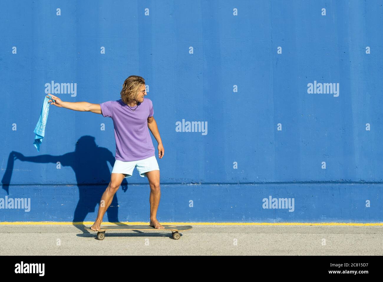 Junge blonde Mann mit blauem Schal gehen auf Skate mit einem blauen Hintergrund. Sommer, Surf-Konzept. Stockfoto