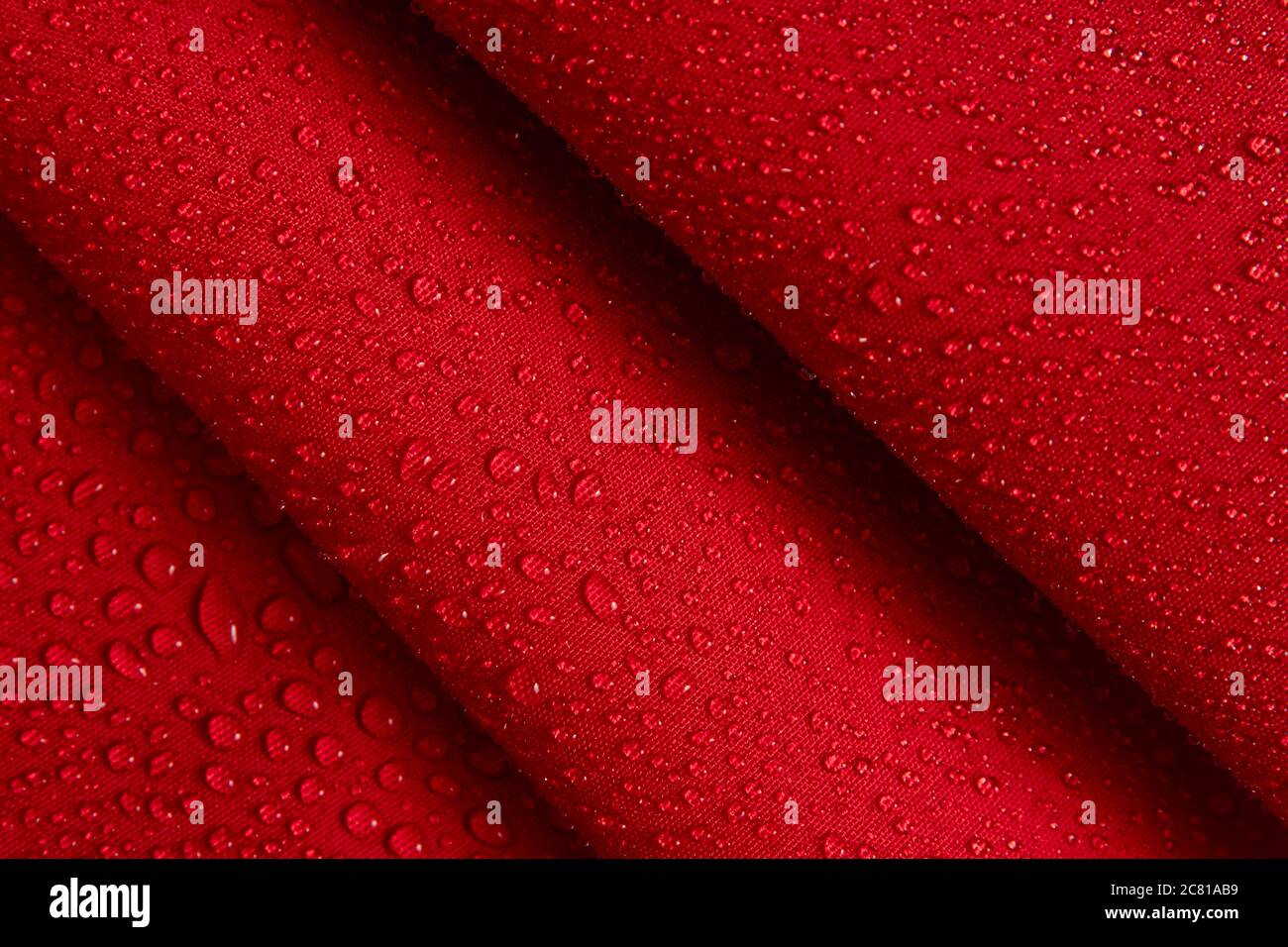 Abstrakter Hintergrund aus hydrophobem Stoff. Wassertropfen auf knittertem rotem Stoff. Stockfoto