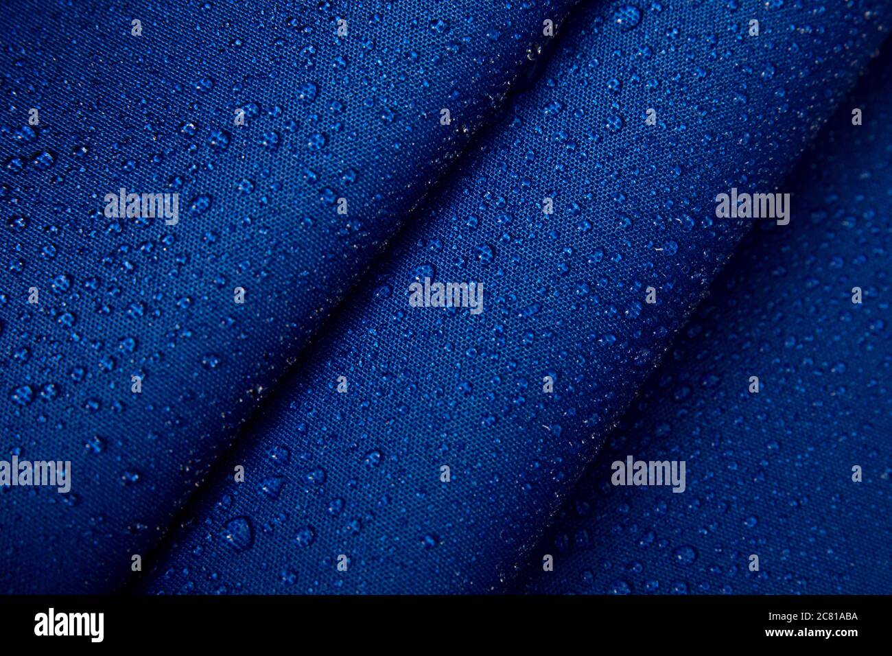 Abstrakter Hintergrund aus hydrophobem Stoff. Wassertropfen auf gefnittertem blauem Stoff. Stockfoto